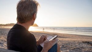 Man journaling in the morning at the beach to reflect and improve wellbeing