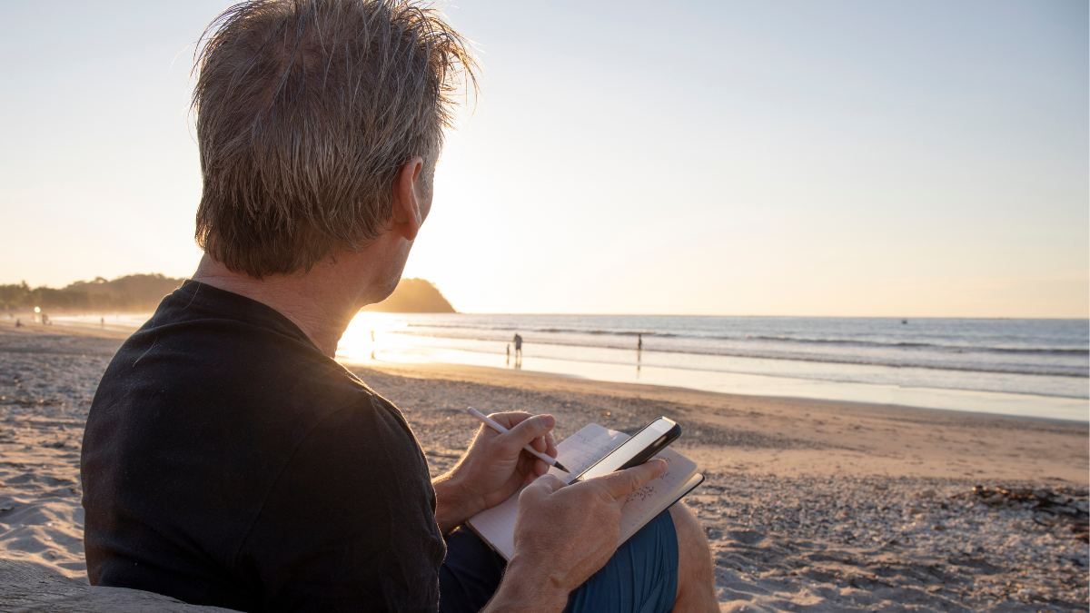 Man journaling in the morning at the beach to reflect and improve wellbeing